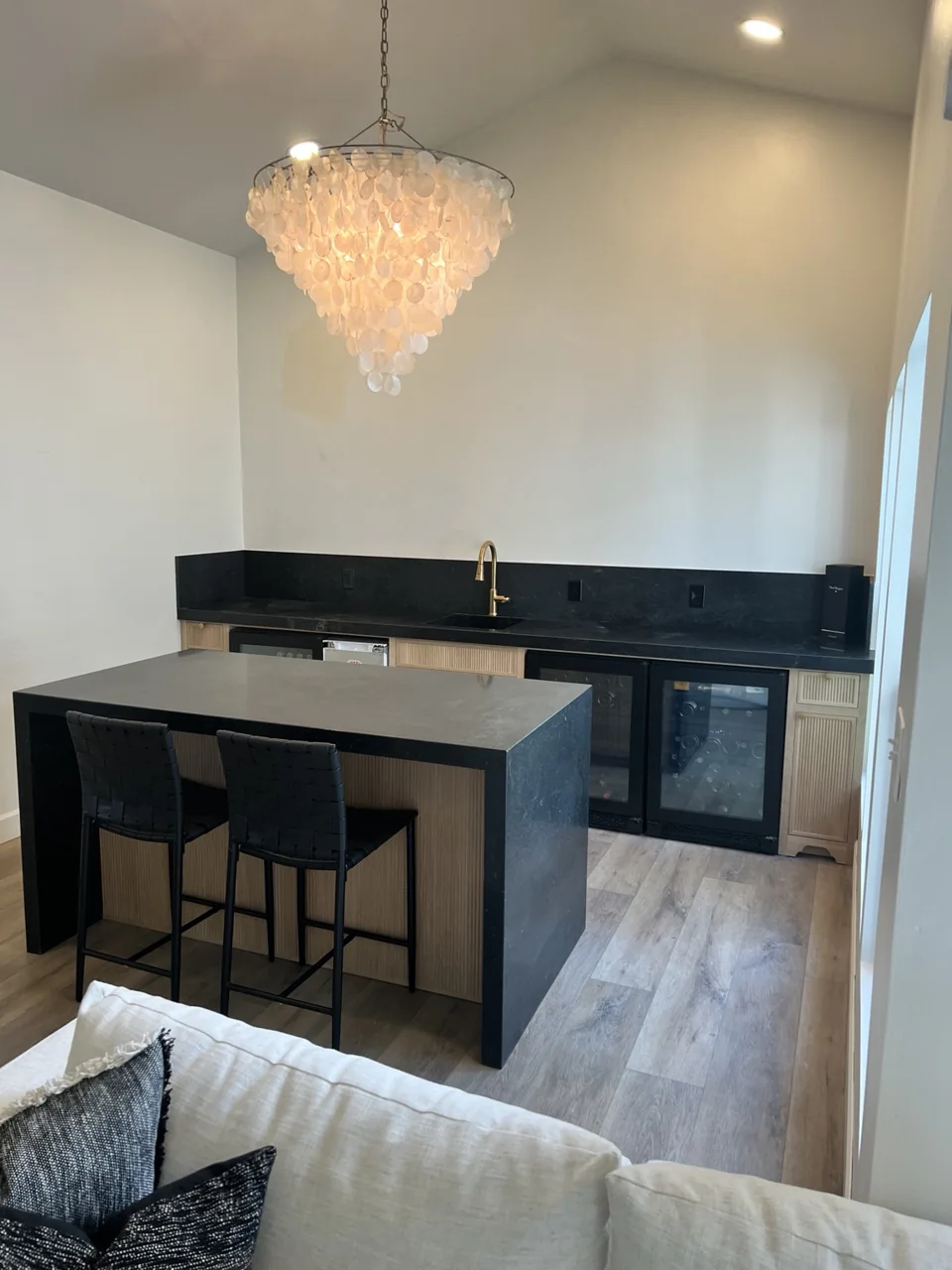 Natural wood cabinetry, dark stone surfaces, and an island create a dedicated beverage space.