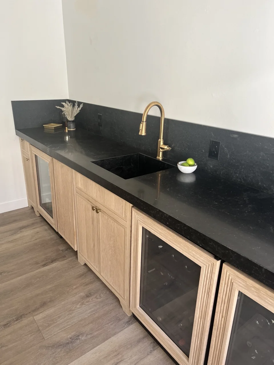 Fluted wood cabinetry, a dark sink and backsplash, and a brushed-gold faucet.