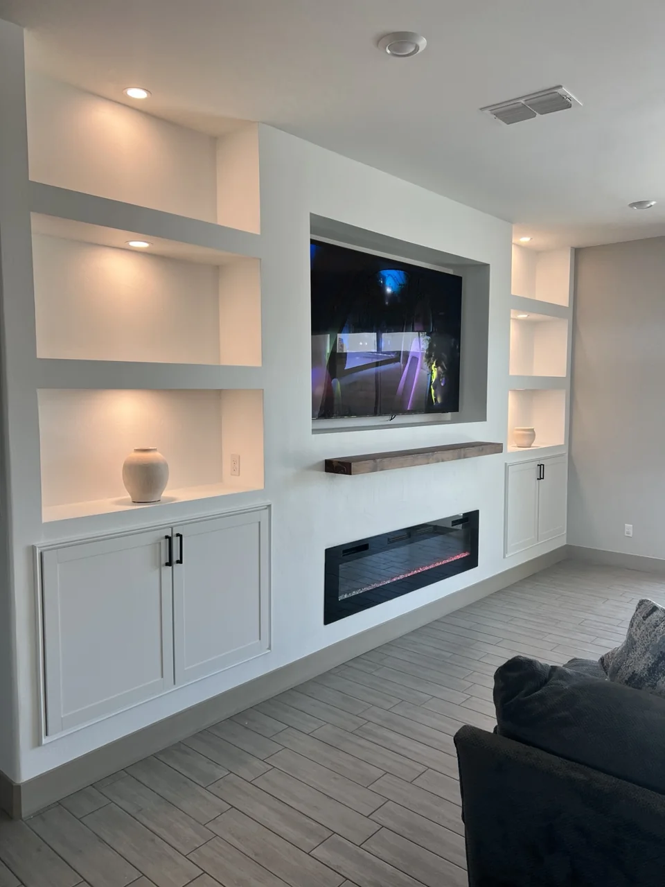 A custom entertainment wall with illuminated shelving, lower cabinetry, and a linear fireplace.