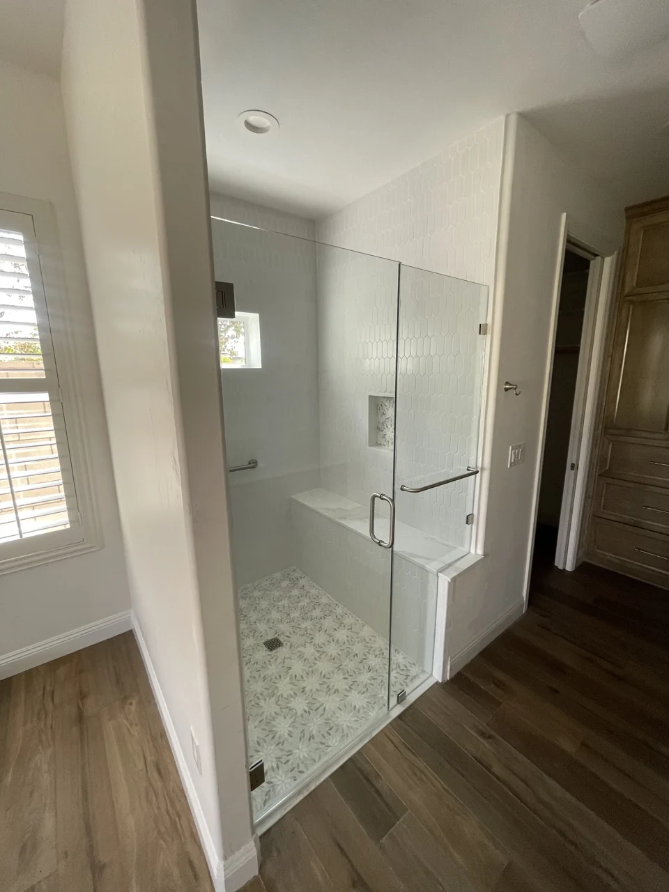 A glass shower enclosure with a tiled bench, recessed niche, and patterned floor.