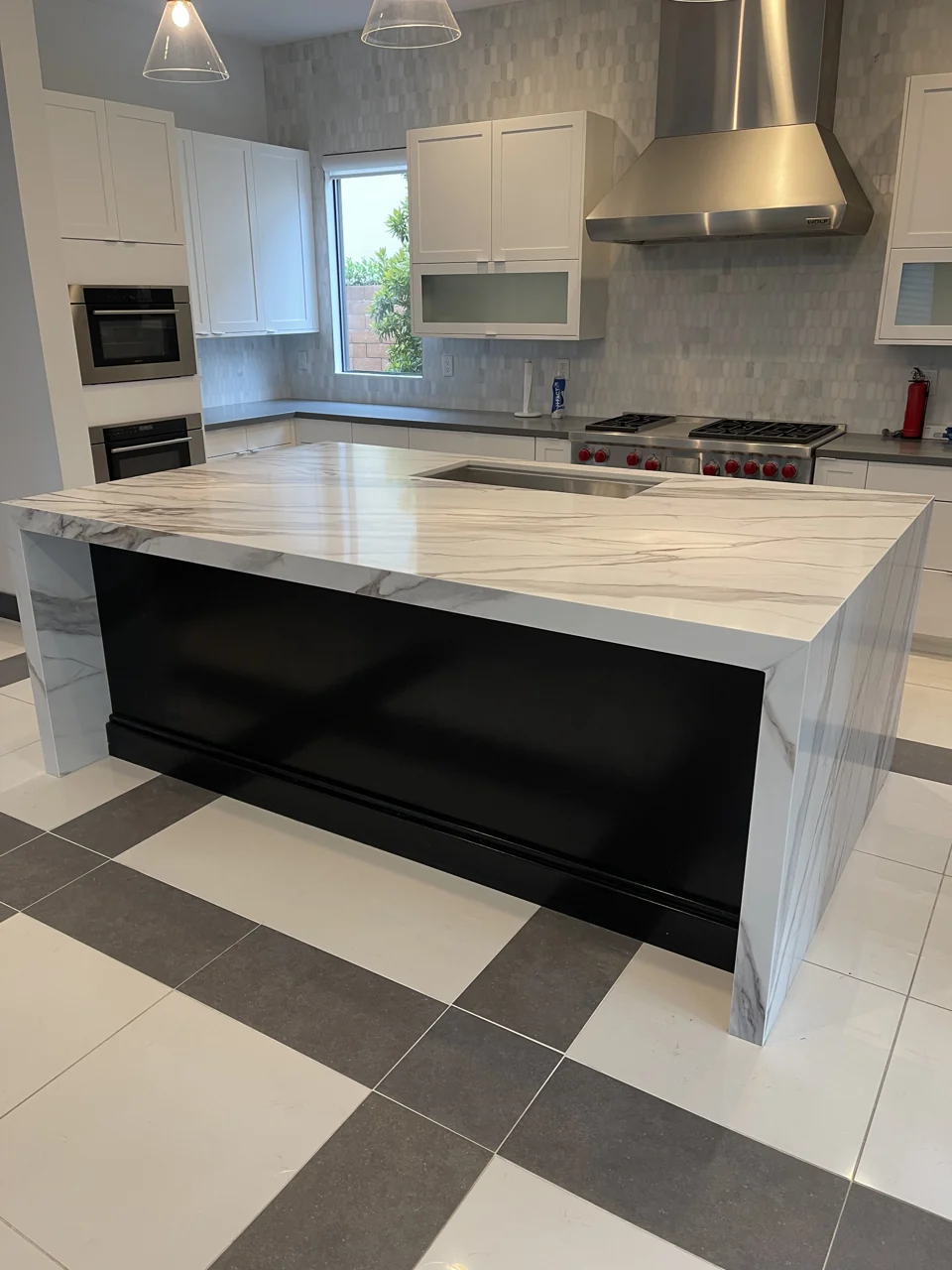 Kitchen finishing in progress: a veined waterfall island and white cabinetry, with final sink fittings still to be completed.