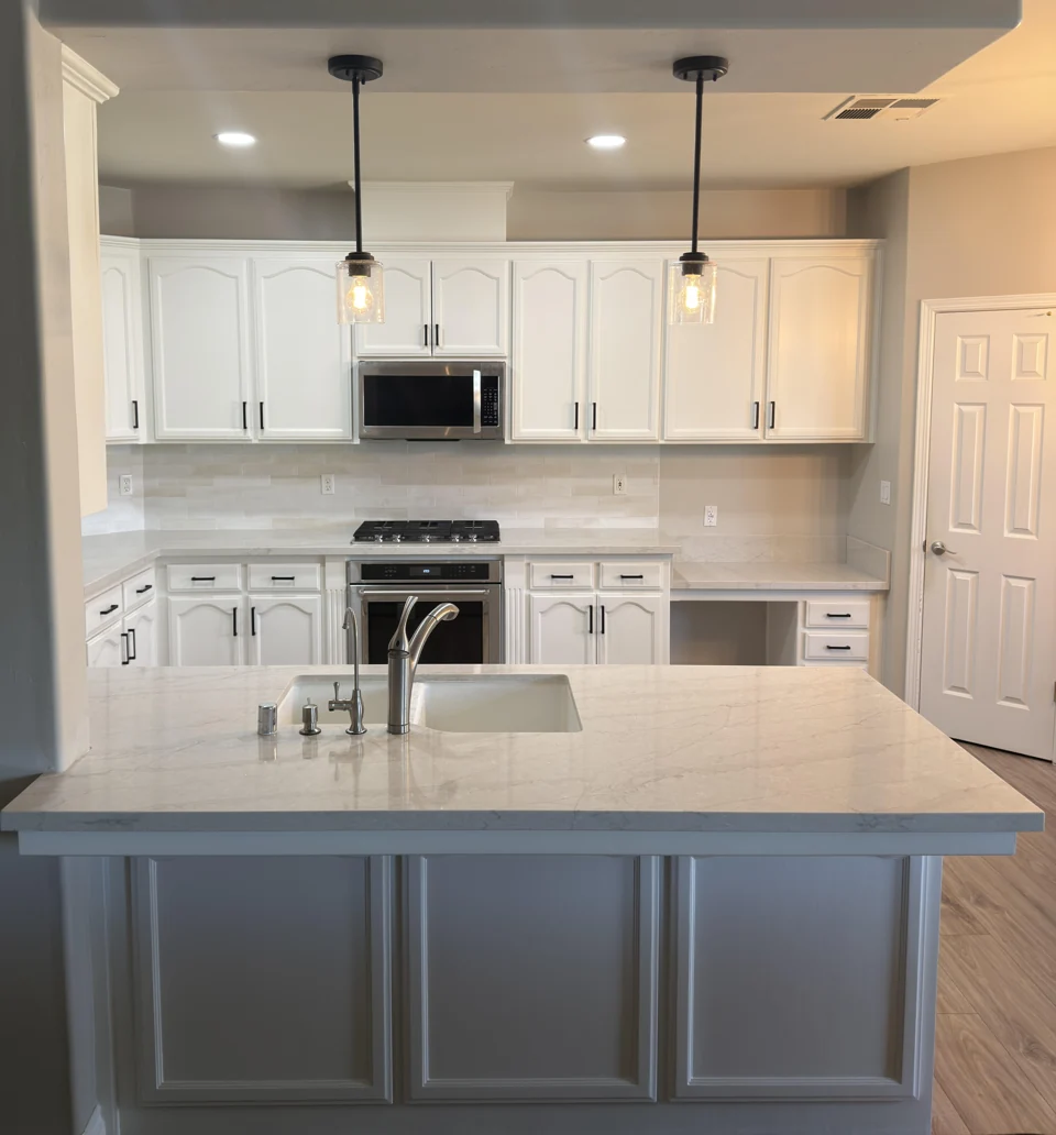 White cabinetry, black hardware, glass pendants, and a stone-topped island.